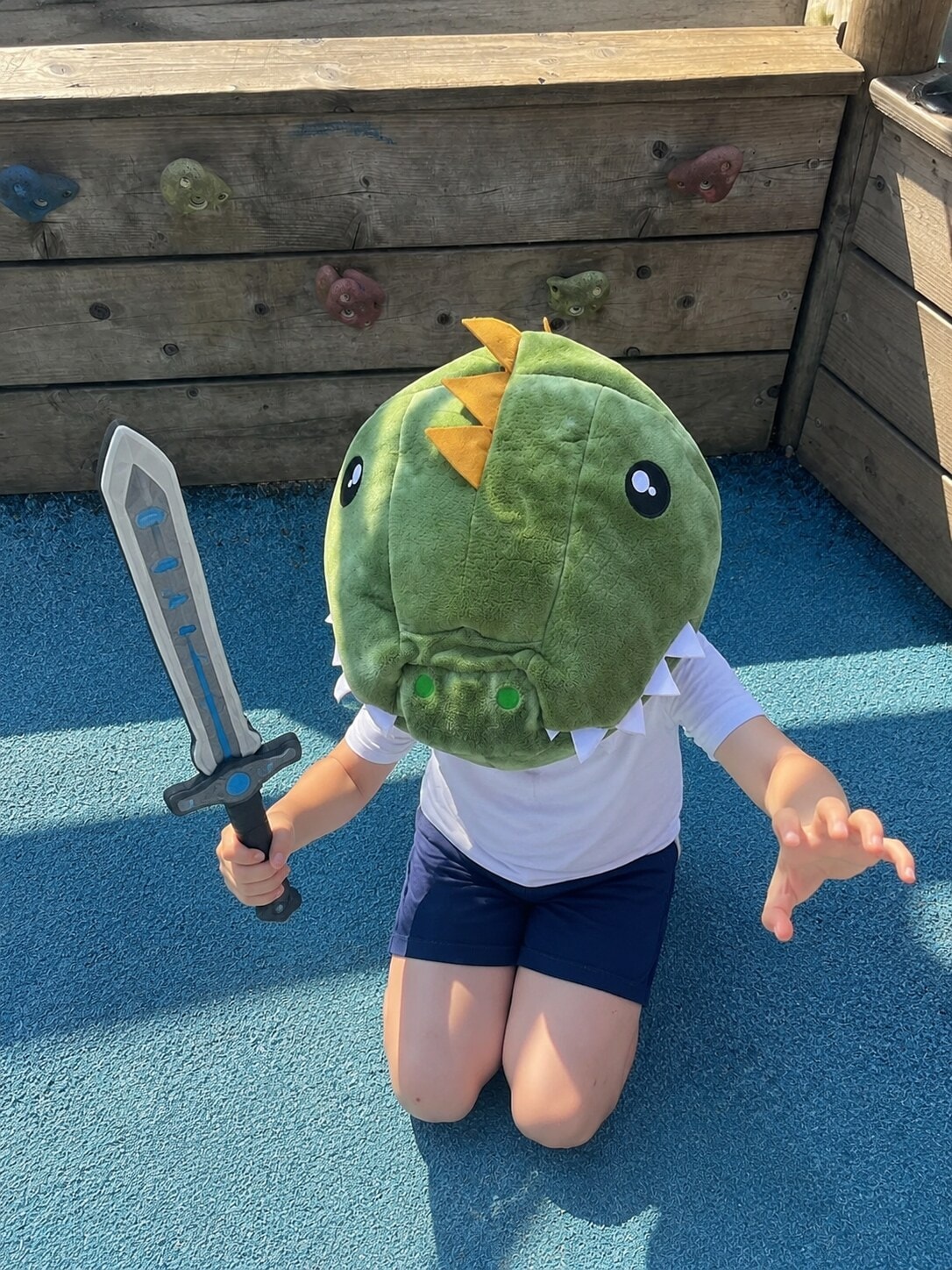 Child wearing a dinosaur costume head with a toy sword during imaginative play