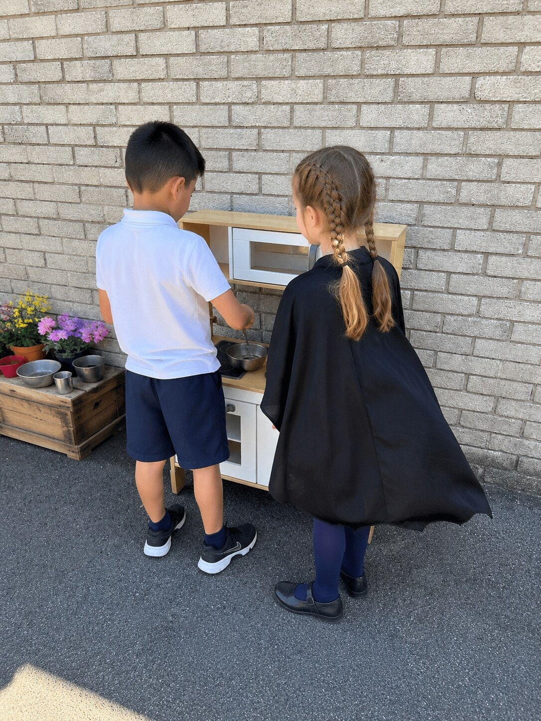 Two children playing together at an outdoor mud kitchen