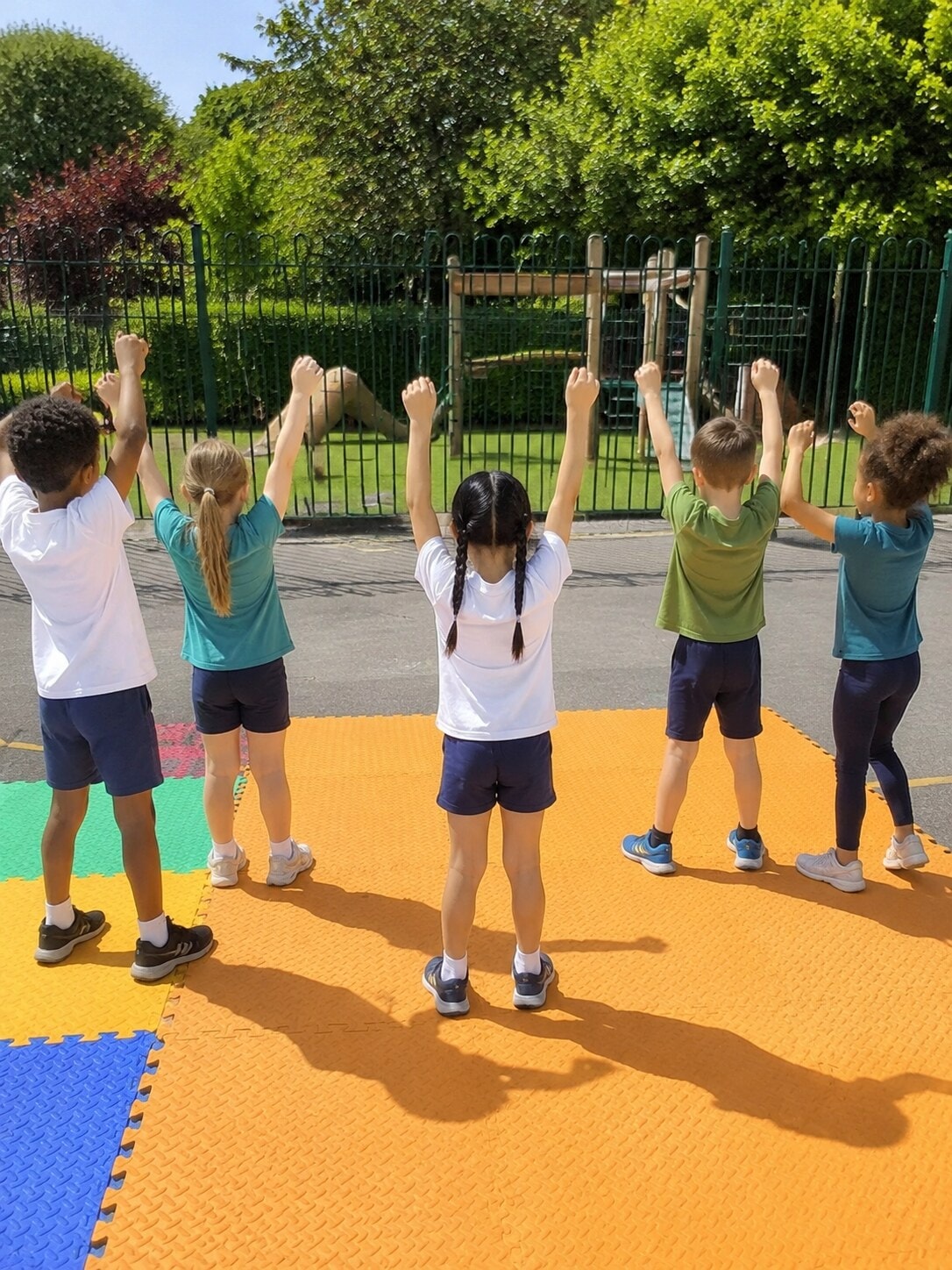 Children raising their arms together in a joyful group stretch on colourful playground mats