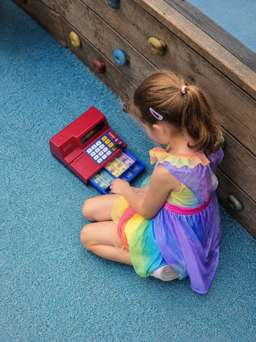 Child in a fairy costume playing with a toy cash register during outdoor pretend shop play
