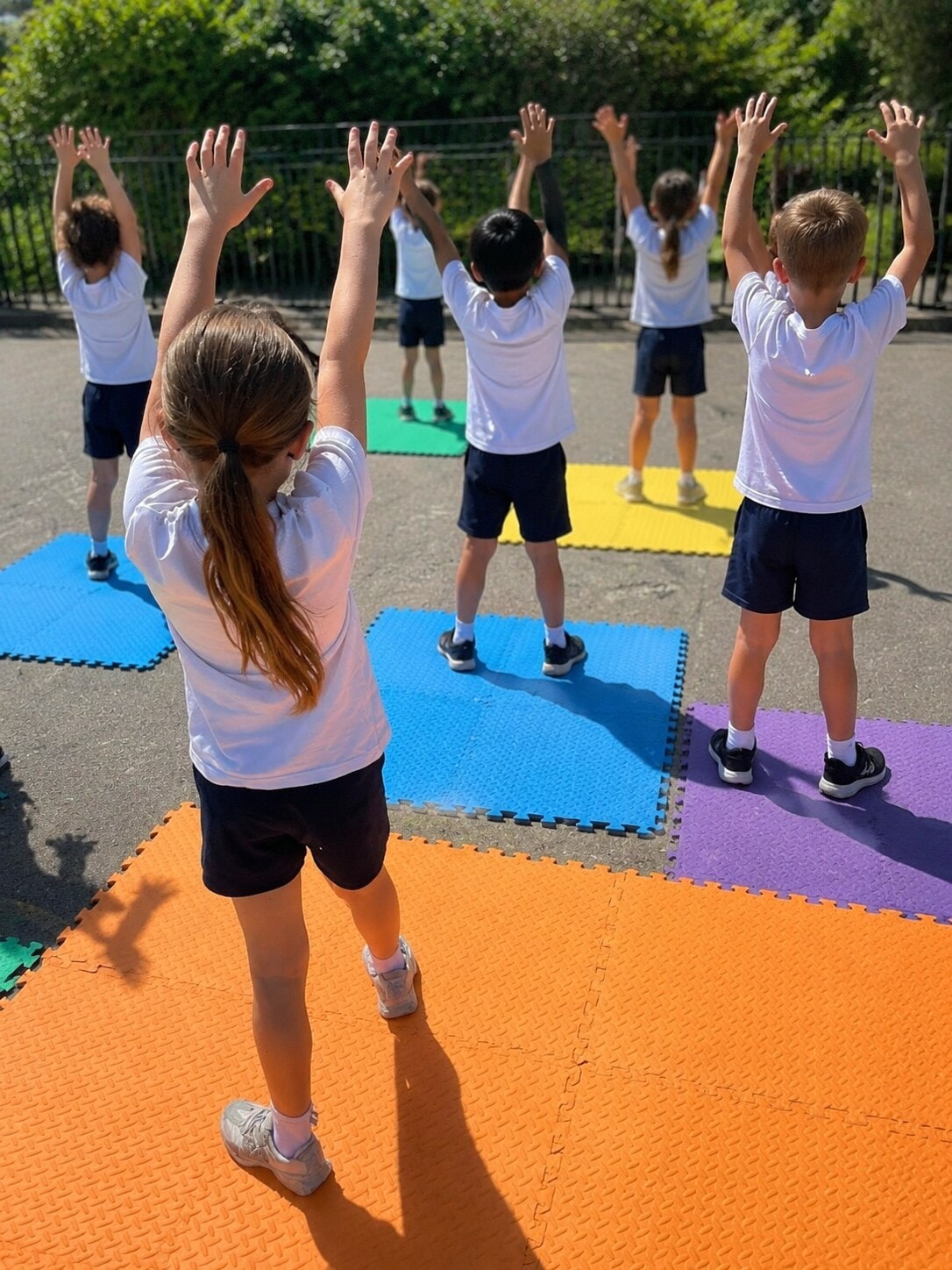 Group of children stretching arms up high while standing on colourful foam mats in the playground