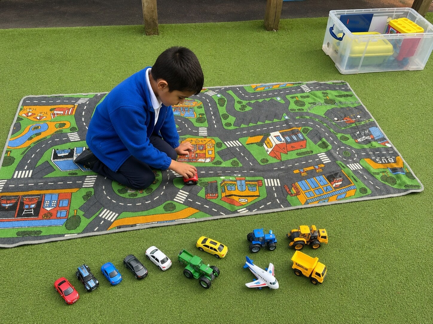 Child playing independently with toy vehicles on a road-themed play mat outdoors