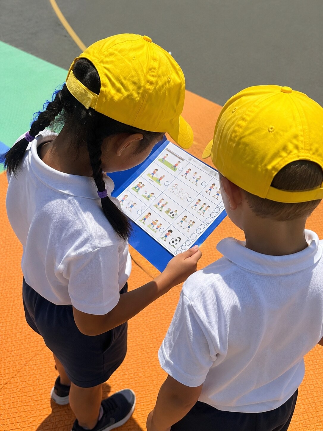 Two play leaders wearing yellow caps studying a clipboard with activity plans in the playground