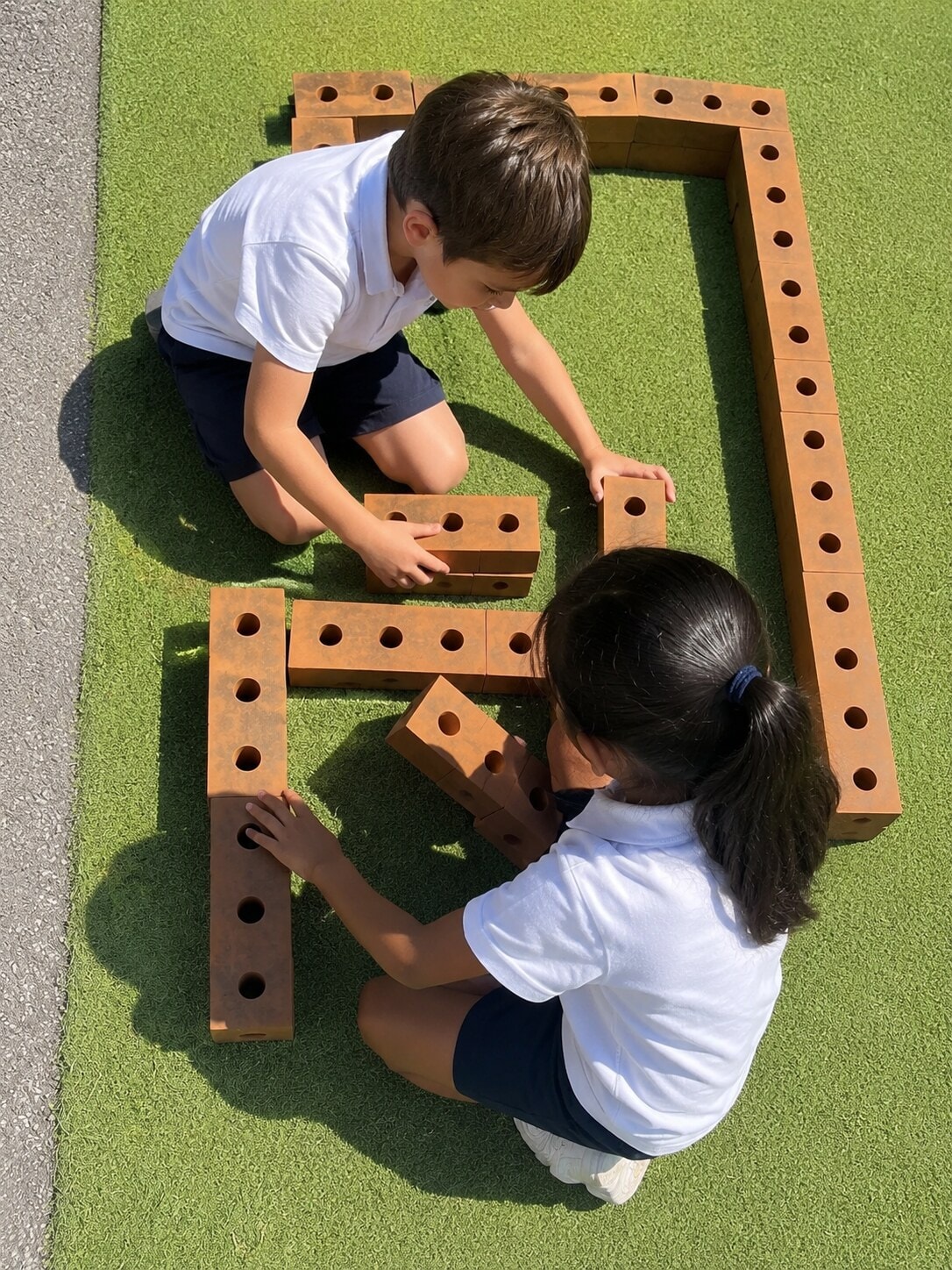 Two children working together to build a structure with large wooden blocks on artificial turf